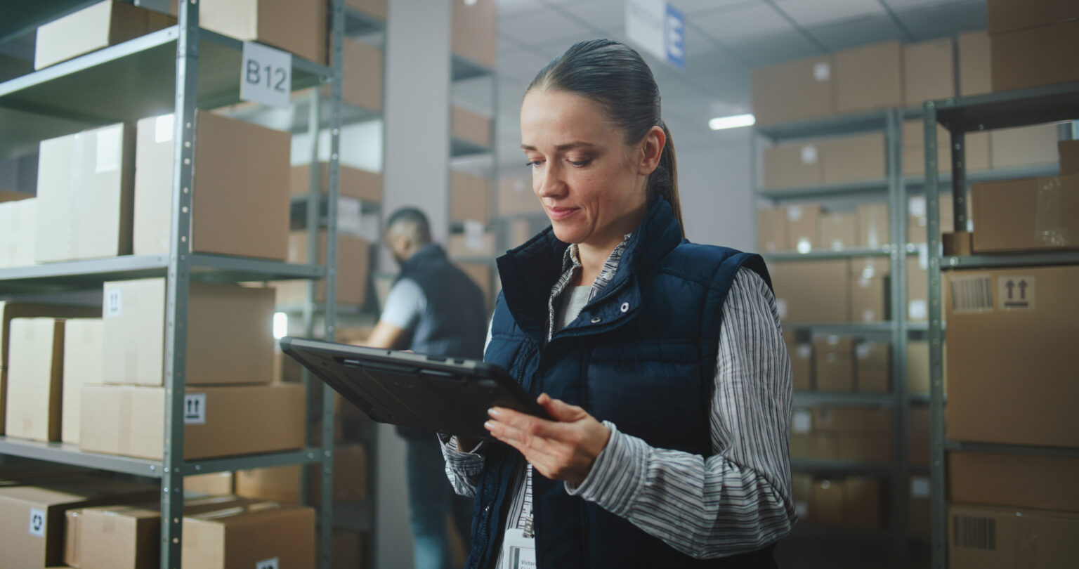Female Inventory Manager in Warehouse Facility: Uses Tablet Computer, Looks at Camera. Sorting Worker Preparing Online Orders for Shipping. Delivery Service, Logistics Distribution Center. Portrait.