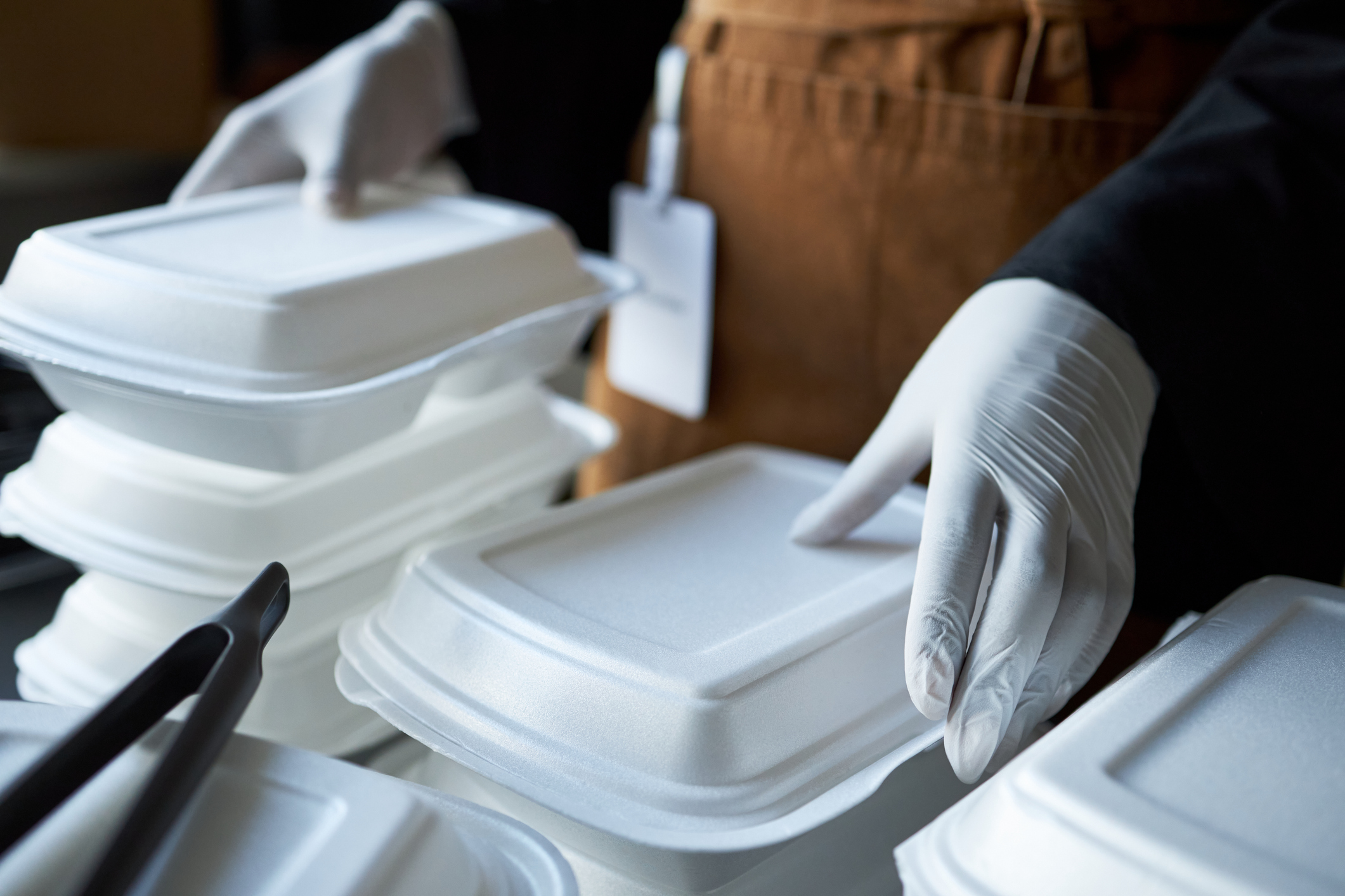 Meal preparation professional wearing gloves handling food containers for packaging and delivery ensuring hygiene and safety standards while stacking containers