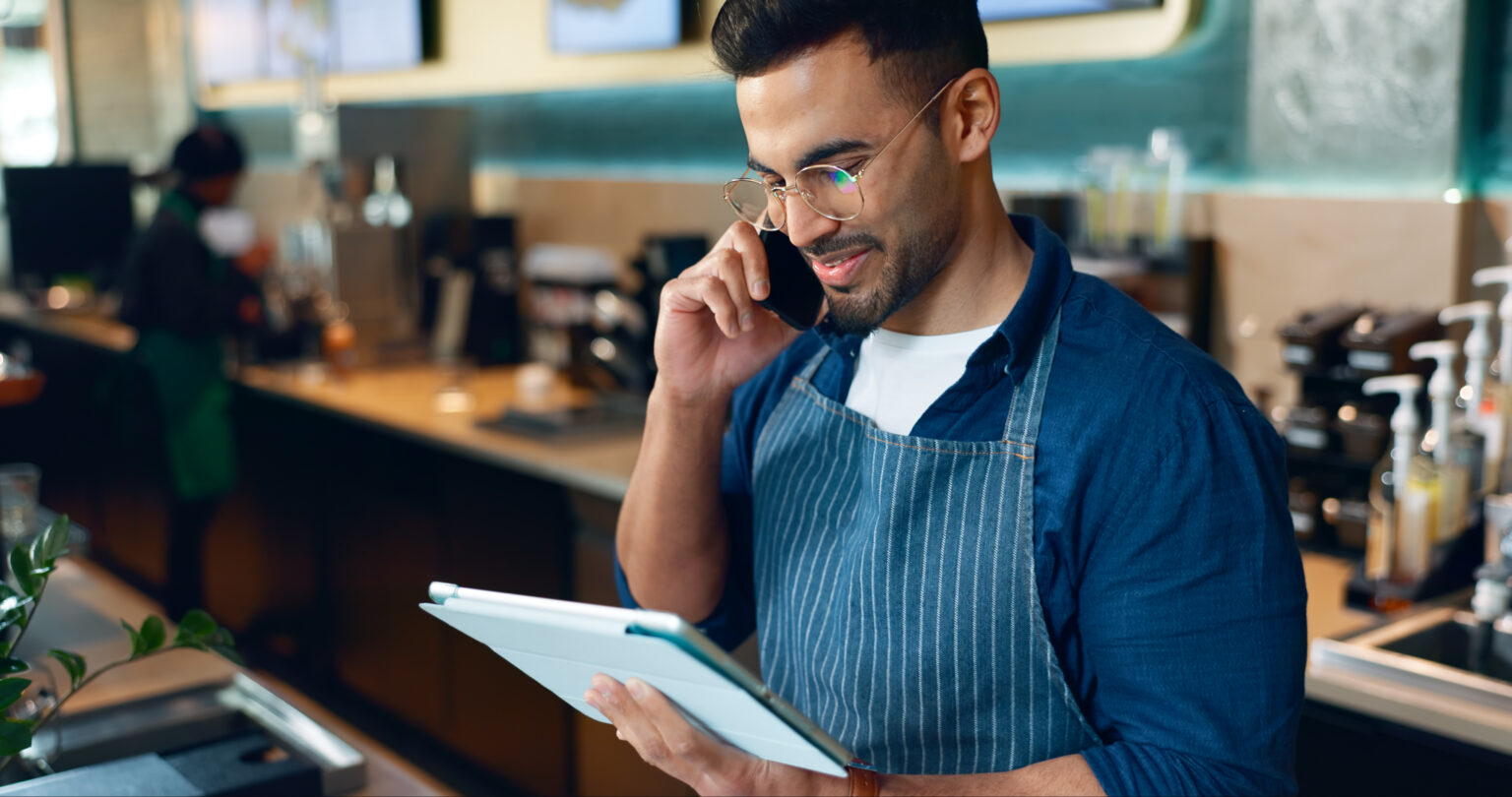 Phone call, restaurant or barista on tablet for small business logistics, social media update or sale. Manager, listen or Indian man reading on technology app for coffee shop order in cafe startup MyOrders by Foodbuy and iTrade